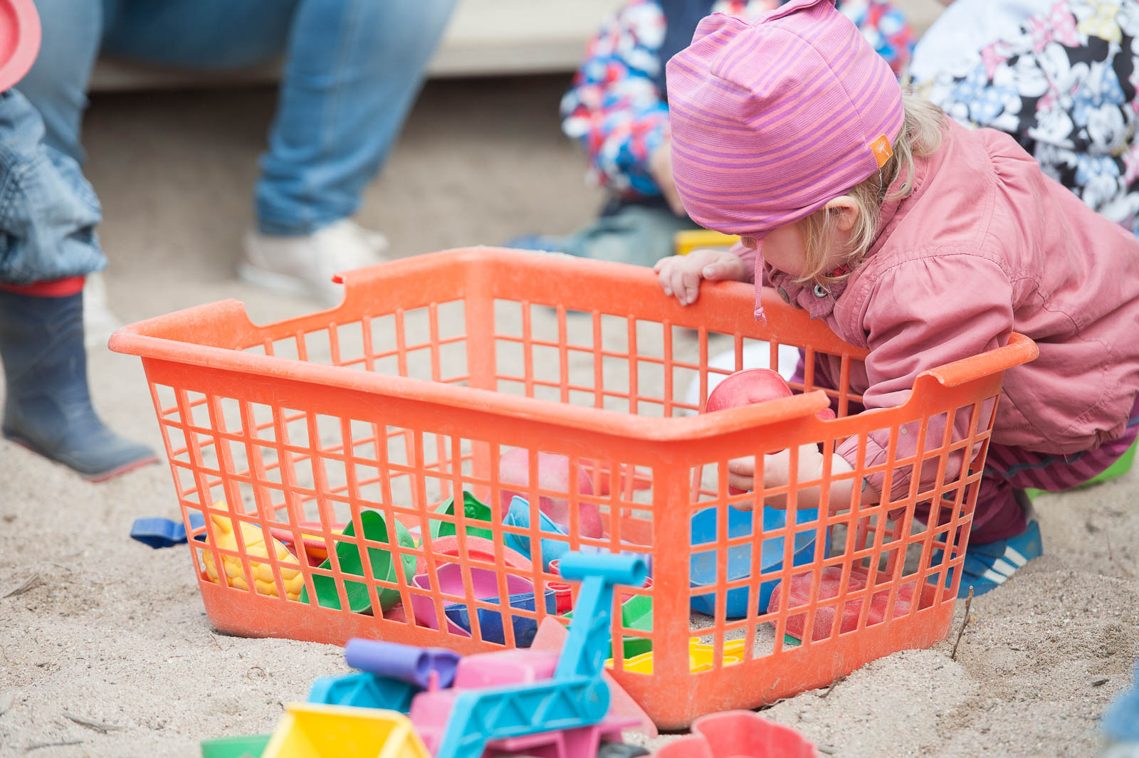 Kind sortiert im Sandkasten Spielzeug aus einer orangefarbenen Kiste